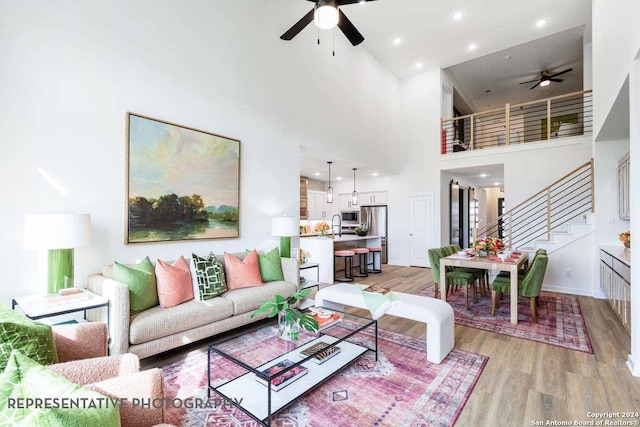 living room with ceiling fan, light hardwood / wood-style flooring, and a high ceiling