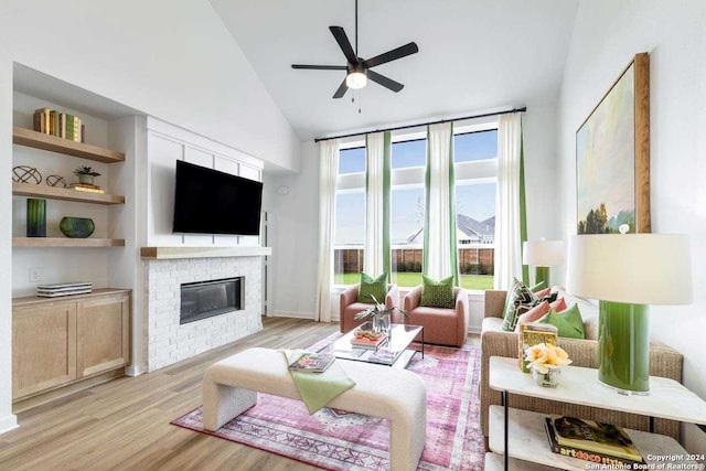 living room featuring a brick fireplace, built in shelves, ceiling fan, high vaulted ceiling, and light hardwood / wood-style floors