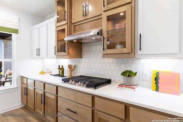 kitchen with stainless steel gas cooktop, tasteful backsplash, hardwood / wood-style floors, white cabinets, and exhaust hood