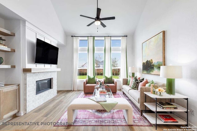 living room with a brick fireplace, ceiling fan, light wood-type flooring, and vaulted ceiling