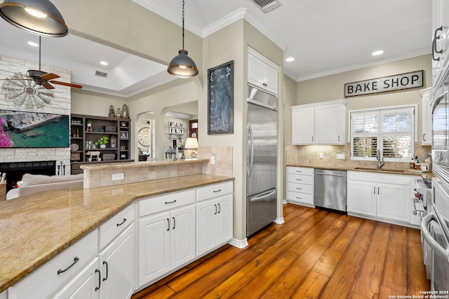 kitchen with white cabinetry, hanging light fixtures, a brick fireplace, kitchen peninsula, and appliances with stainless steel finishes