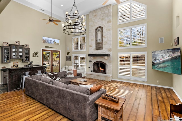 living room with ceiling fan with notable chandelier, french doors, a towering ceiling, and a stone fireplace