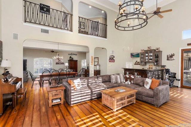 living room featuring hardwood / wood-style floors, ceiling fan with notable chandelier, ornamental molding, and a high ceiling