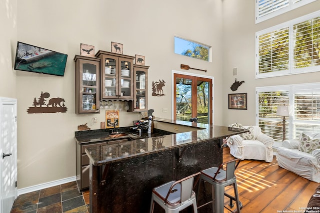 bar with dark stone countertops, dark brown cabinetry, french doors, and a high ceiling