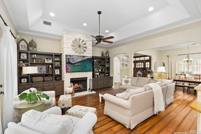 living room with ceiling fan with notable chandelier, a tray ceiling, crown molding, a fireplace, and dark hardwood / wood-style floors