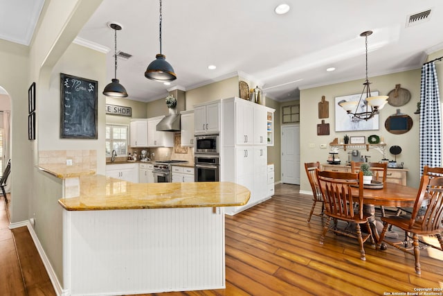 kitchen with wall chimney exhaust hood, hanging light fixtures, stainless steel appliances, tasteful backsplash, and kitchen peninsula