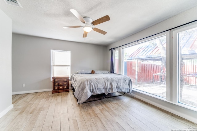 bedroom with ceiling fan, light hardwood / wood-style floors, and a textured ceiling