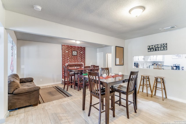 dining space featuring a brick fireplace, a textured ceiling, and light wood-type flooring