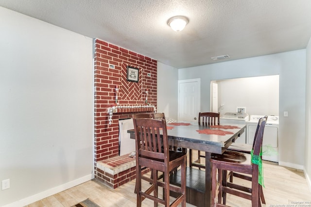 dining room featuring a textured ceiling, light wood-type flooring, separate washer and dryer, and a brick fireplace