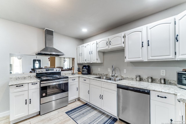 kitchen featuring wall chimney exhaust hood, stainless steel appliances, sink, light hardwood / wood-style flooring, and white cabinets