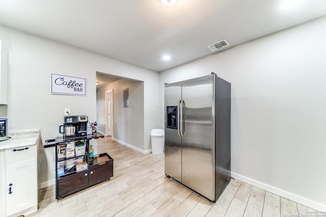 kitchen with stainless steel fridge, light wood-type flooring, and white cabinetry