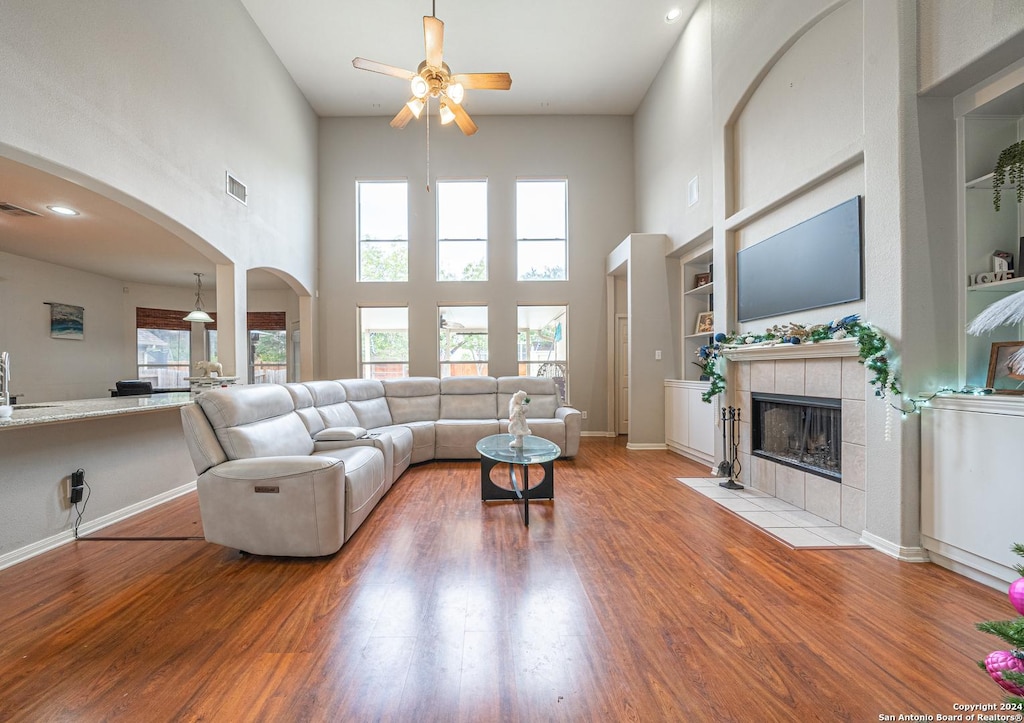 living room with built in shelves, light hardwood / wood-style floors, a towering ceiling, and a wealth of natural light