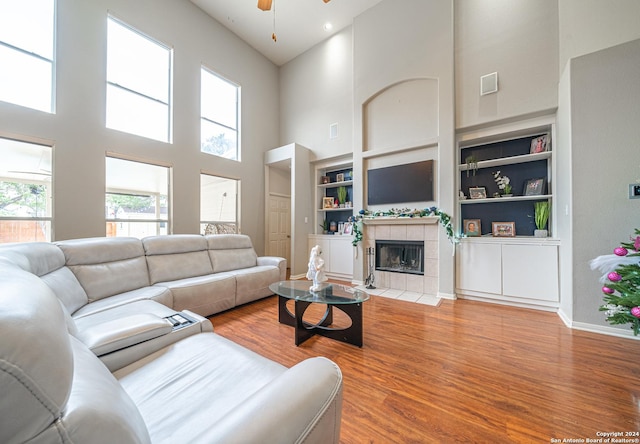 living room featuring ceiling fan, a high ceiling, built in features, light hardwood / wood-style floors, and a fireplace