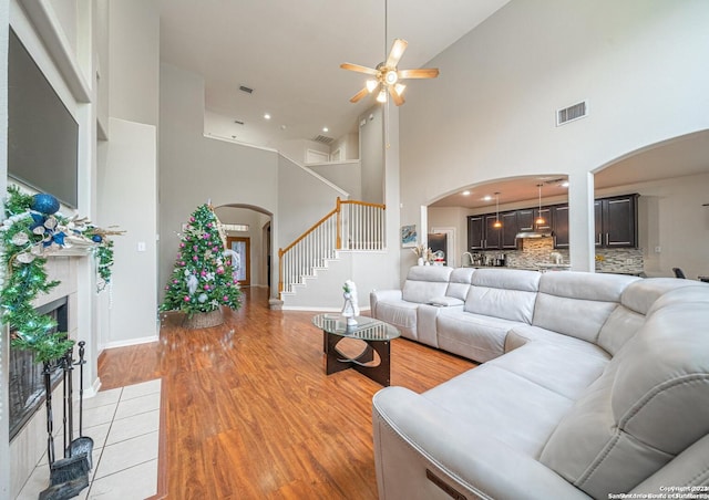 living room with ceiling fan, a towering ceiling, and light hardwood / wood-style floors