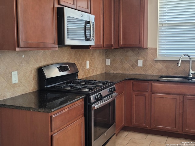 kitchen featuring decorative backsplash, stainless steel appliances, sink, dark stone countertops, and light tile patterned flooring