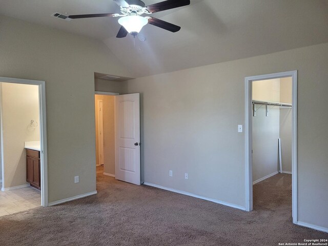 unfurnished bedroom with ensuite bath, a spacious closet, light colored carpet, and vaulted ceiling