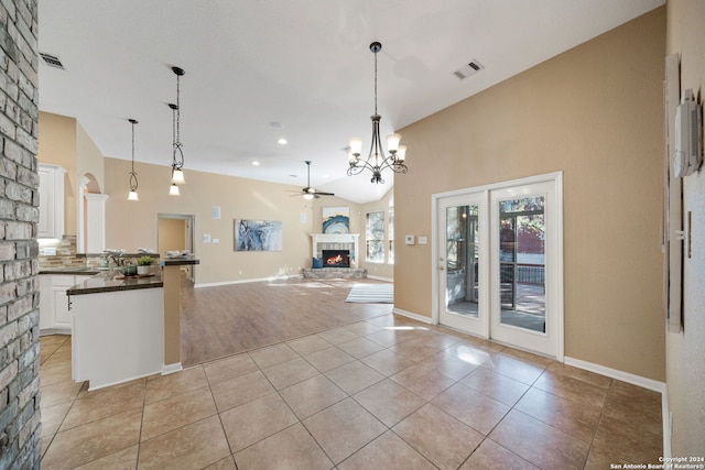 kitchen featuring ceiling fan with notable chandelier, vaulted ceiling, light tile patterned floors, a large fireplace, and white cabinetry