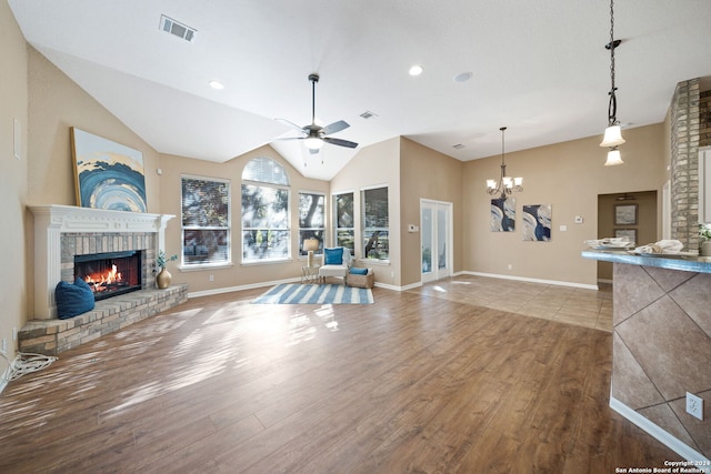 living room featuring a brick fireplace, ceiling fan with notable chandelier, vaulted ceiling, and light hardwood / wood-style flooring