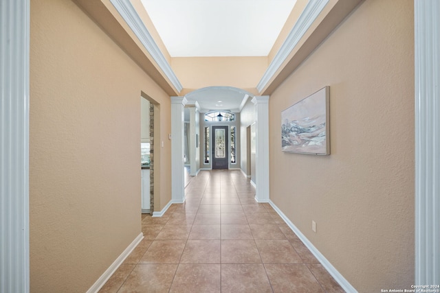 corridor featuring light tile patterned floors, decorative columns, and crown molding