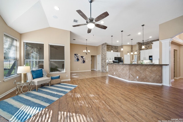 living room featuring hardwood / wood-style floors, ceiling fan with notable chandelier, lofted ceiling, and decorative columns