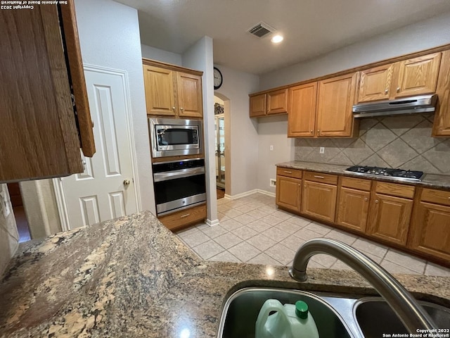 kitchen featuring decorative backsplash, dark stone counters, stainless steel appliances, sink, and light tile patterned floors