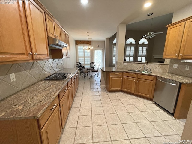 kitchen with sink, stainless steel appliances, pendant lighting, stone countertops, and ceiling fan with notable chandelier