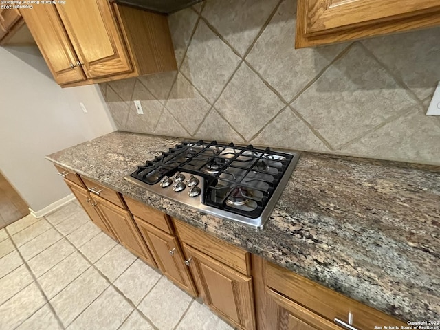 kitchen featuring tasteful backsplash, dark stone countertops, light tile patterned floors, and stainless steel gas stovetop