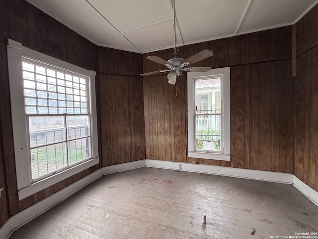 unfurnished room featuring wood walls, ceiling fan, a healthy amount of sunlight, and light wood-type flooring