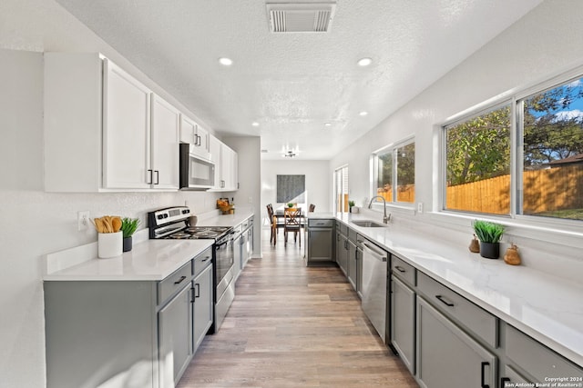 kitchen featuring appliances with stainless steel finishes, gray cabinetry, a textured ceiling, sink, and light hardwood / wood-style floors