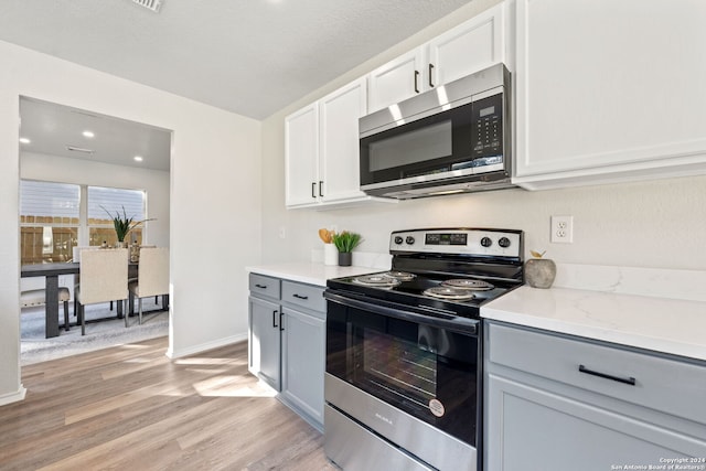 kitchen featuring light stone counters, light hardwood / wood-style flooring, gray cabinets, white cabinets, and appliances with stainless steel finishes