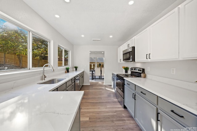 kitchen featuring white cabinetry, sink, stainless steel appliances, light stone counters, and light hardwood / wood-style flooring