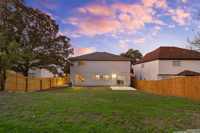 back house at dusk featuring central air condition unit, a patio area, and a lawn