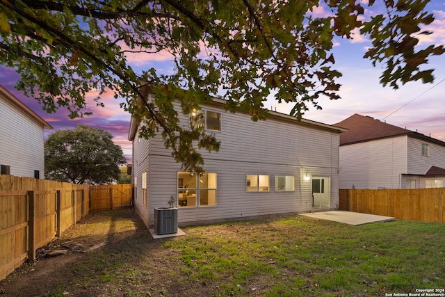 back house at dusk with a yard, a patio, and cooling unit