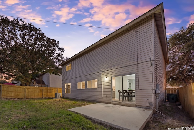 back house at dusk with a lawn, a patio area, and central AC unit