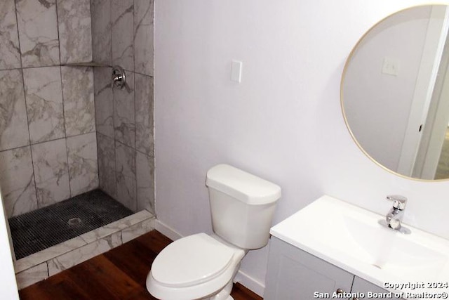 bathroom with hardwood / wood-style flooring, toilet, a tile shower, and vanity