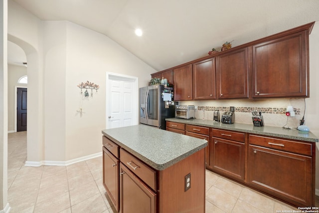 kitchen featuring stainless steel fridge, backsplash, vaulted ceiling, light tile patterned floors, and a center island