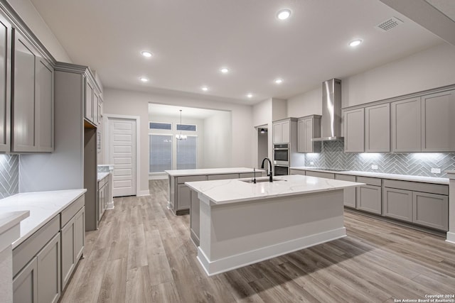 kitchen with wall chimney exhaust hood, gray cabinets, light wood-type flooring, and sink