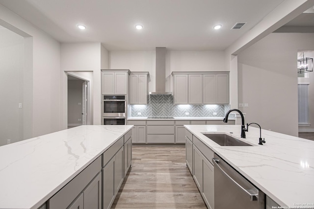 kitchen with gray cabinets, wall chimney range hood, sink, and appliances with stainless steel finishes