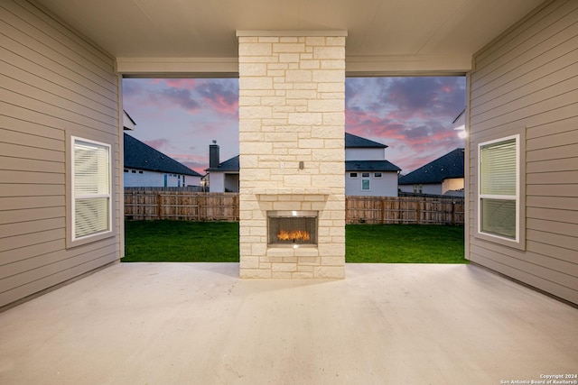 patio terrace at dusk with an outdoor stone fireplace and a yard