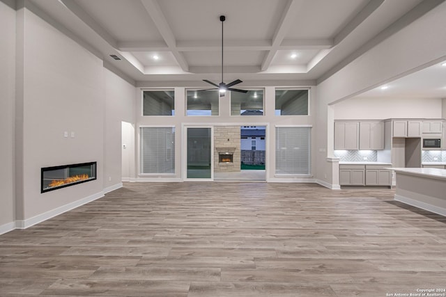 unfurnished living room with beam ceiling, ceiling fan, coffered ceiling, and light wood-type flooring