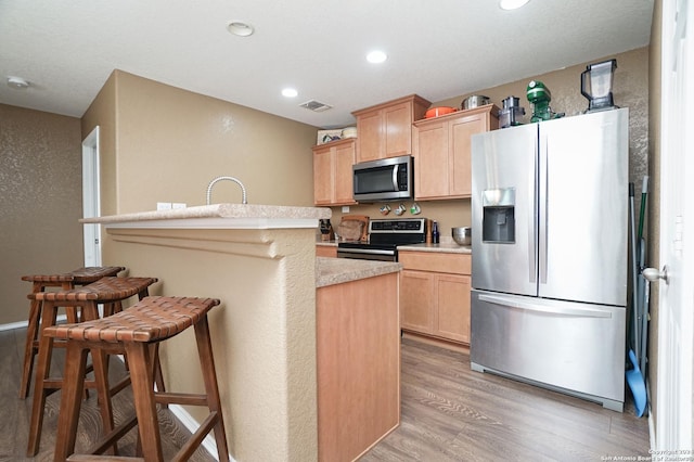 kitchen featuring light brown cabinets, an island with sink, a breakfast bar area, appliances with stainless steel finishes, and light wood-type flooring