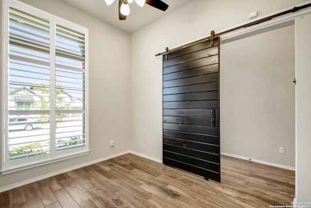 unfurnished room featuring a barn door, ceiling fan, plenty of natural light, and light wood-type flooring