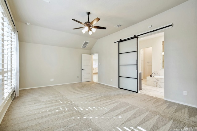 unfurnished bedroom with ensuite bath, ceiling fan, a barn door, light colored carpet, and vaulted ceiling