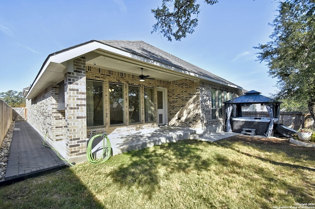 rear view of property featuring ceiling fan, a gazebo, a patio area, a hot tub, and a lawn