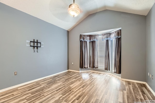 spare room featuring a textured ceiling, wood-type flooring, and lofted ceiling