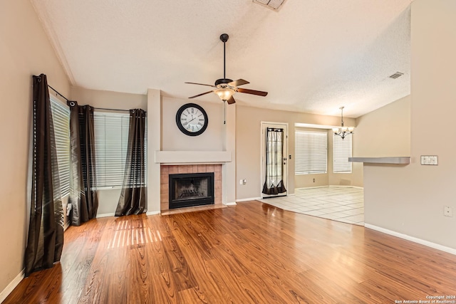 unfurnished living room with a tiled fireplace, light hardwood / wood-style flooring, ceiling fan with notable chandelier, and a textured ceiling