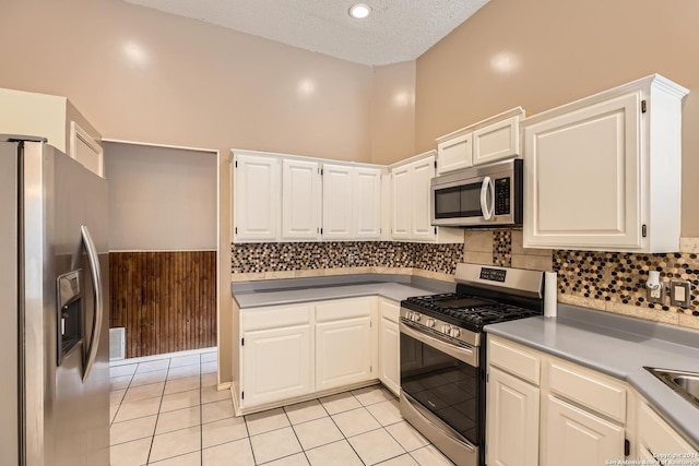 kitchen with appliances with stainless steel finishes, a textured ceiling, light tile patterned floors, white cabinetry, and wood walls