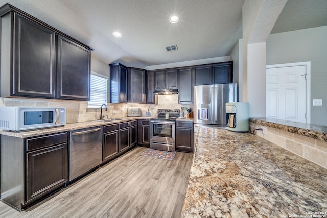 kitchen with backsplash, light stone counters, stainless steel appliances, sink, and light hardwood / wood-style flooring