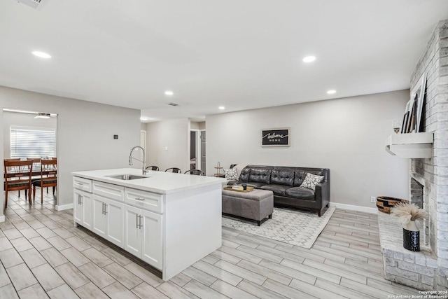 4911 Dare, San Antonio, TX 78217 - kitchen featuring white cabinets, sink, light hardwood / wood-style flooring, a brick fireplace, and an island with sink