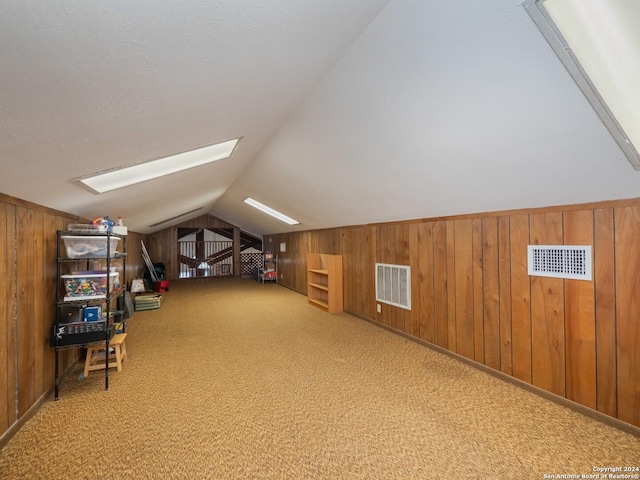 additional living space featuring carpet, lofted ceiling with skylight, and wooden walls